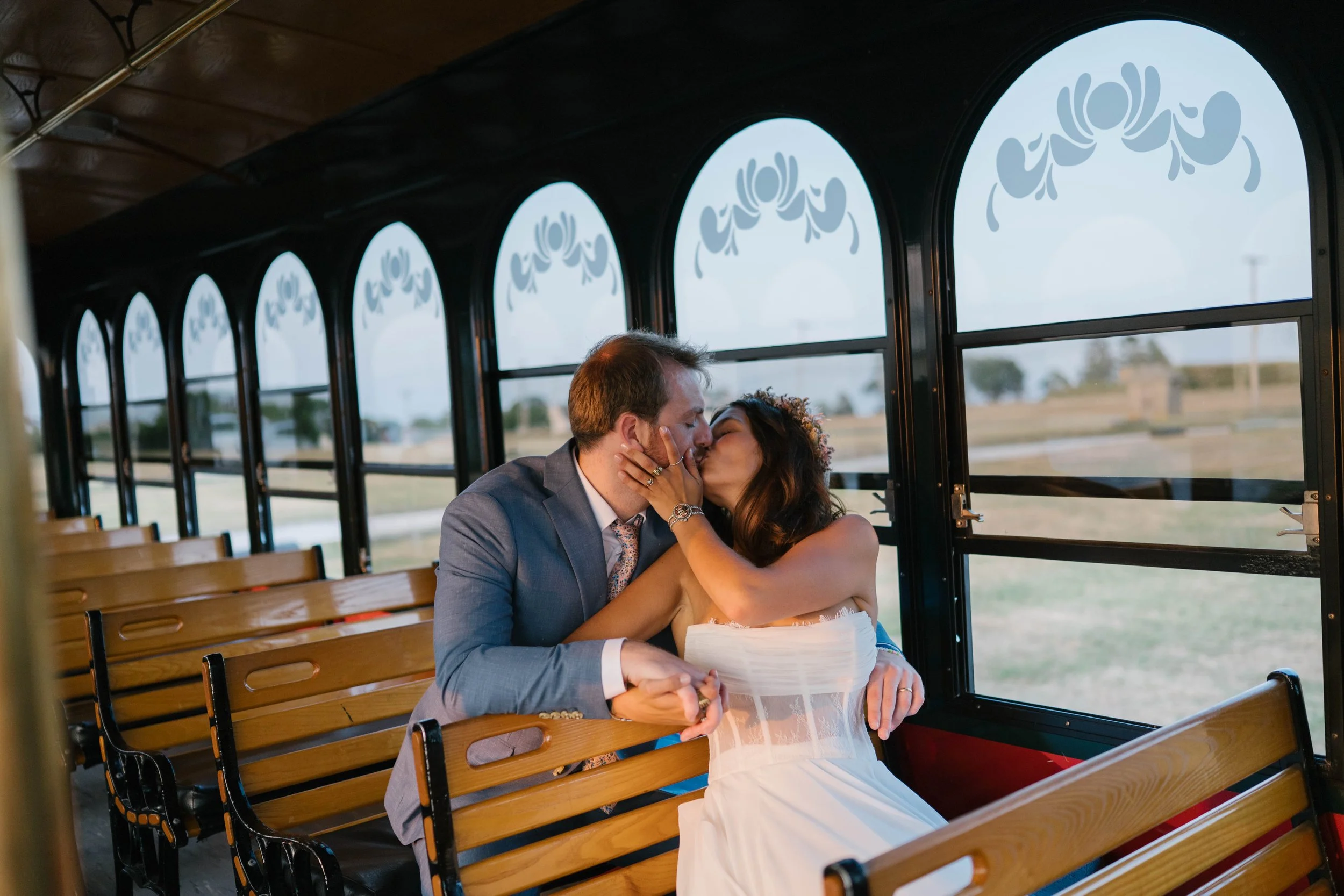 A couple sharing a kiss inside a vintage trolley with stained glass windows and wooden interior.