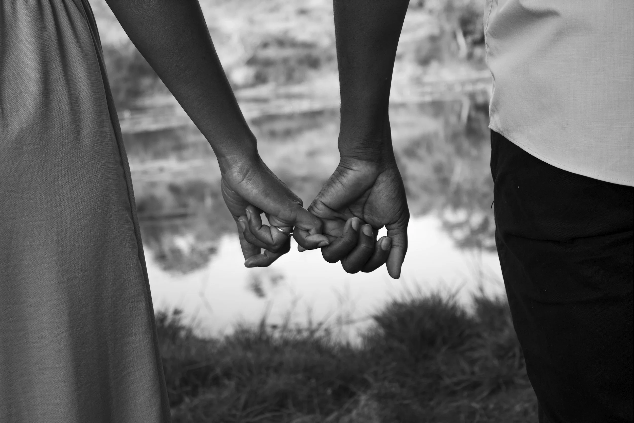 Close-up of two people holding hands, black and white outdoor setting.