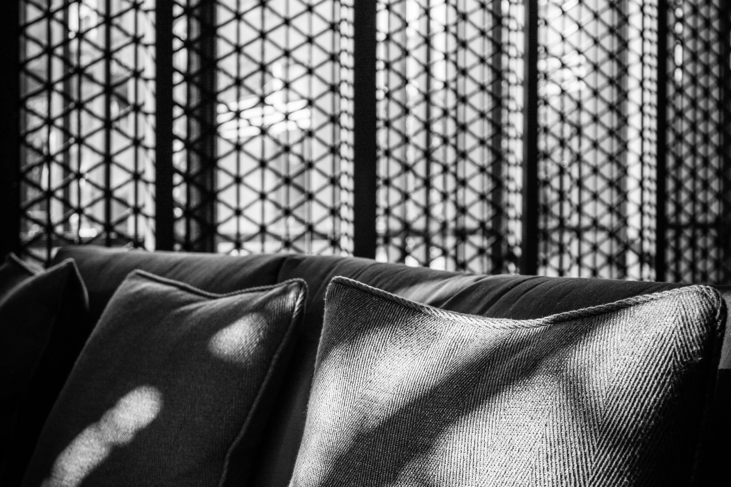Black and white photograph of a sofa with pillows in front of a large window with a geometric grid pattern in a therapy office in South Florida.