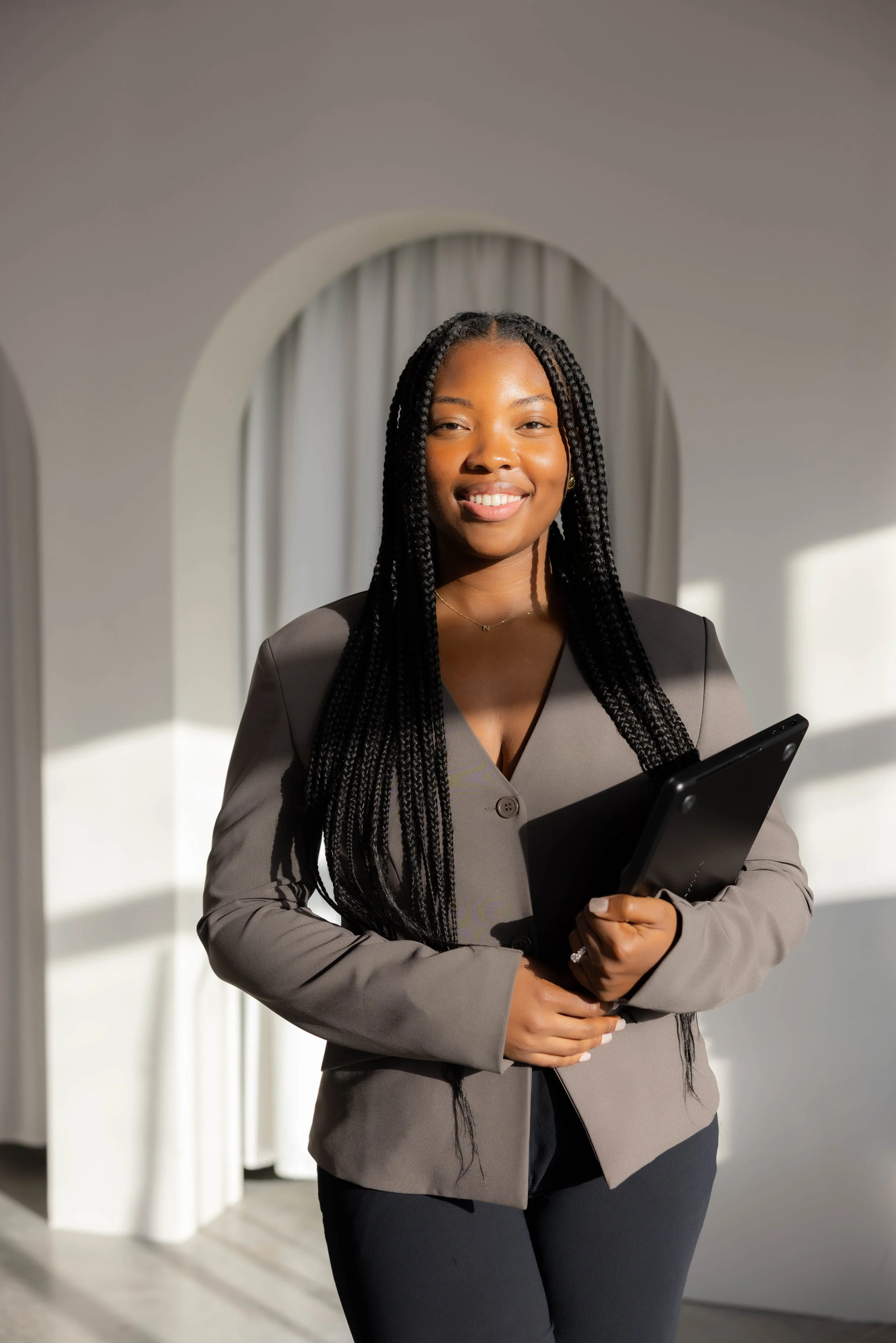 A professional woman smiling in an office, holding a tablet, with soft natural light offering anxiety and traua  therapy in Fort Lauderdale, Florida.