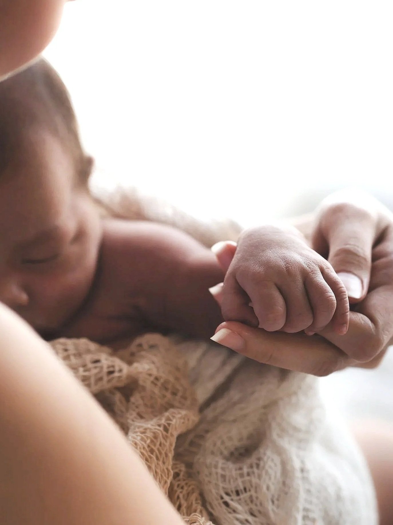 Un bébé endormi et une main adulte tenant la sienne, avec un fond clair et lumineux.