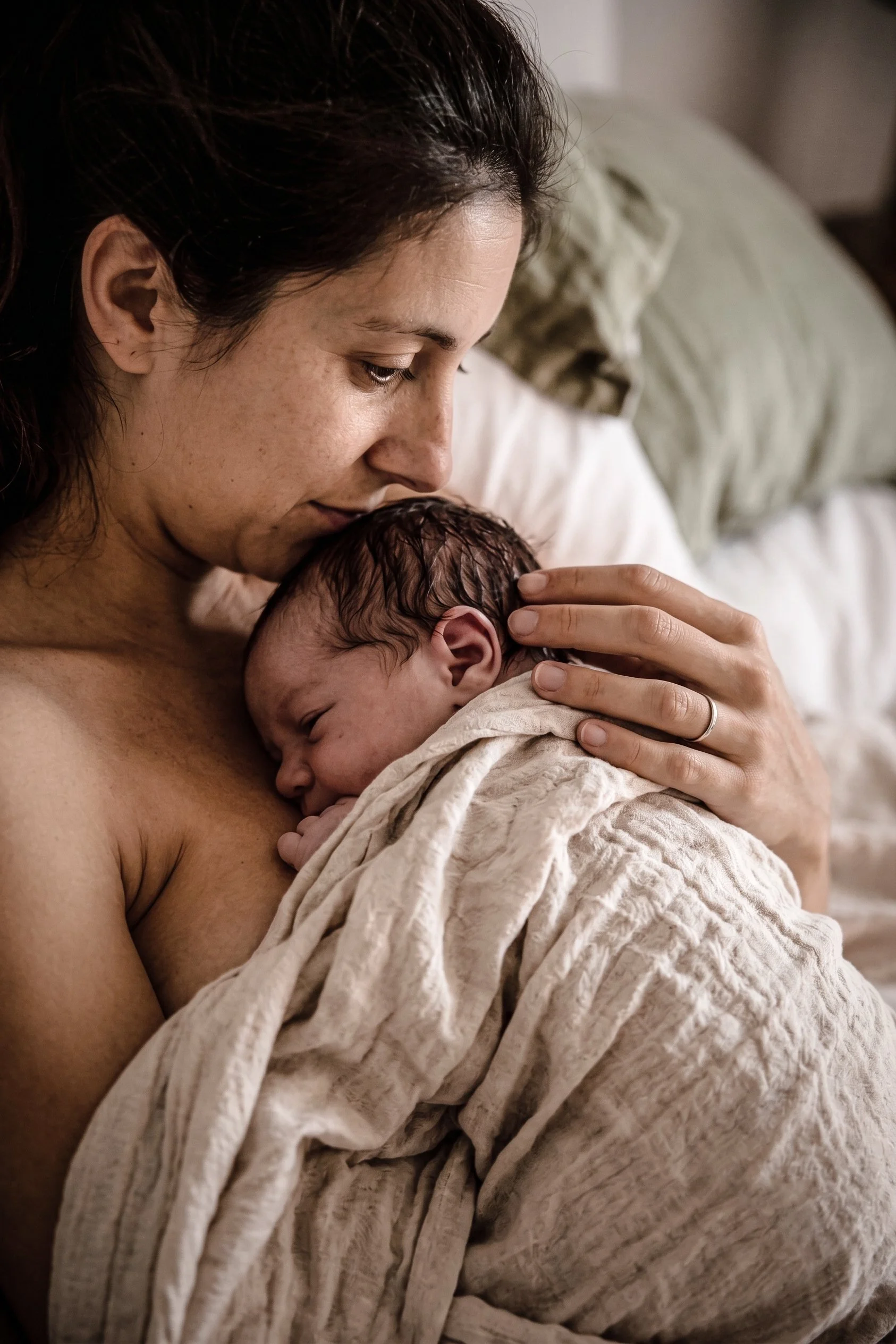 Une mère tient son nouveau-né contre elle, la tête du bébé reposant sur sa poitrine, dans un environnement calme et intime.