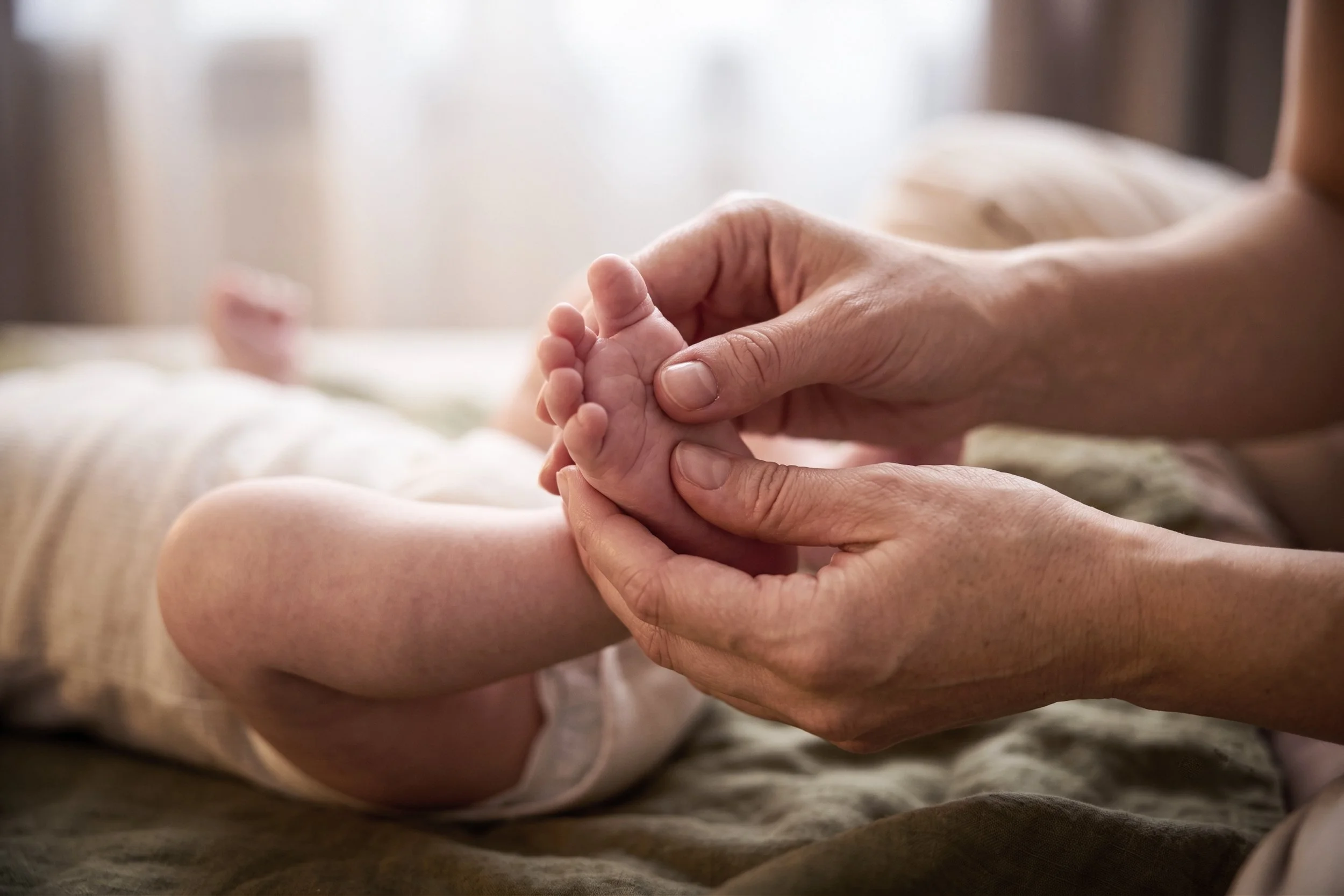 Une main d'adulte tenant doucement la petite main d'un bébé.