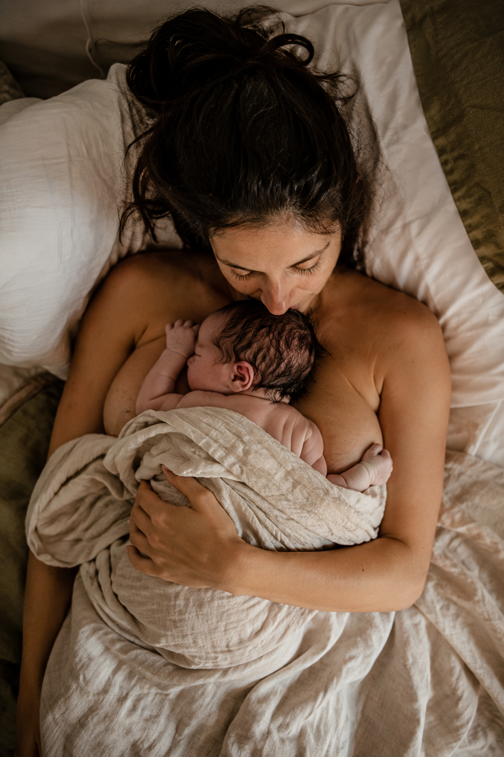 Une femme allongée dans un lit, tenant un bébé nouveau-né contre elle, partageant un moment tendre et intime.