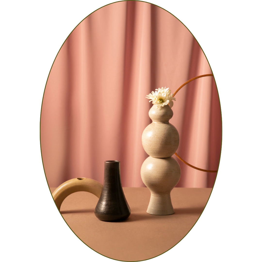 Decorative vases and a flower on a table with pink curtains in the background.