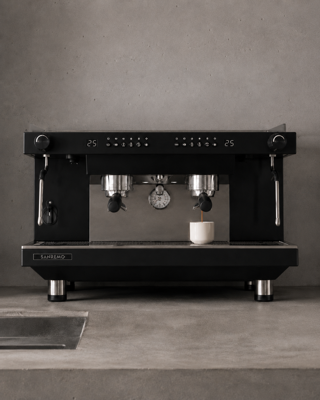 Black espresso machine on gray kitchen counter with a mug underneath the spout and a cup storing espresso.