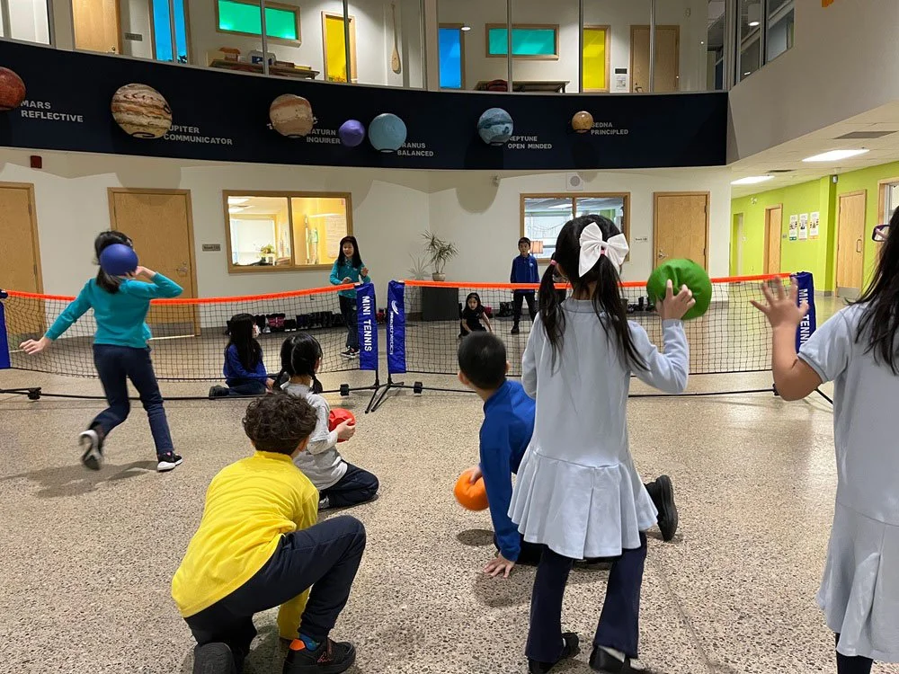 Children playing a game of indoor volleyball with soft balls in a colorful school or activity center.
