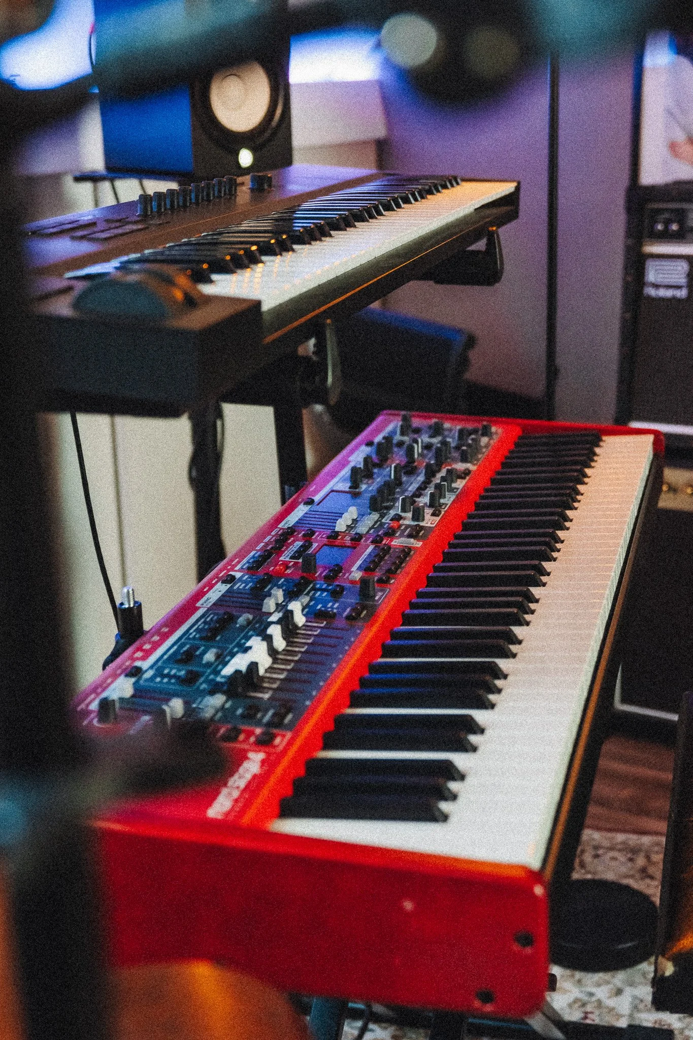 Een rood elektronisch keyboard op een standaard, met een ander keyboard erboven. In de achtergrond zijn studio-monitoren zichtbaar.