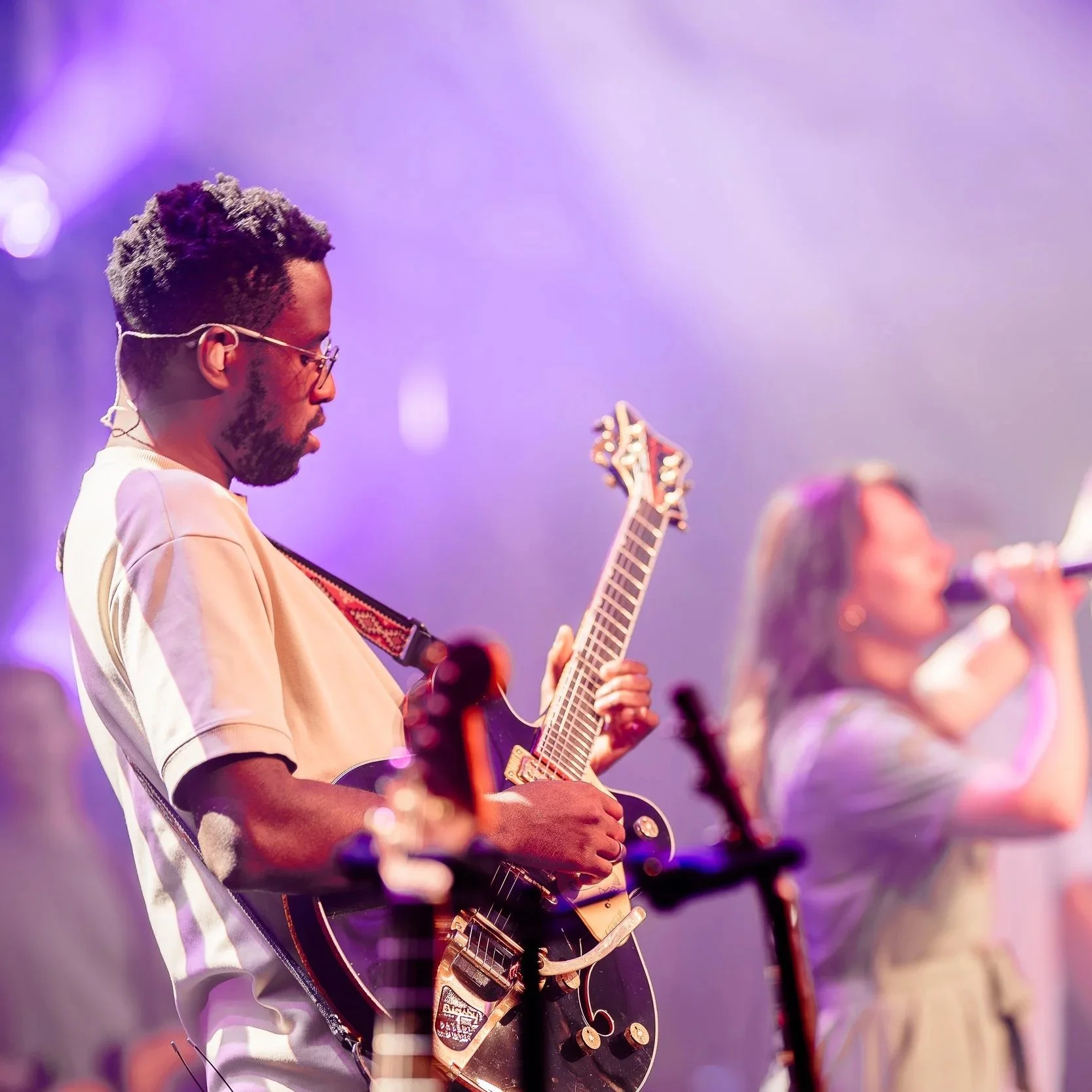 Man speelt elektrische gitaar tijdens een live muziekoptreden in een sfeervolle, kleurrijke setting.