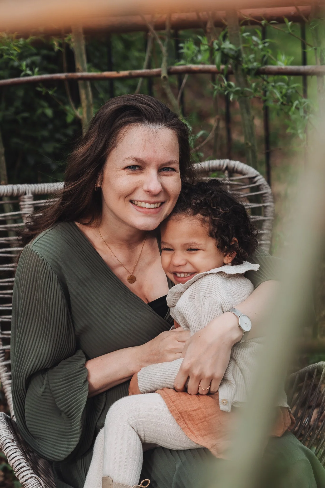 Een vrouw en een kind op een schommel in een groene tuin, lachend en knuffelend.