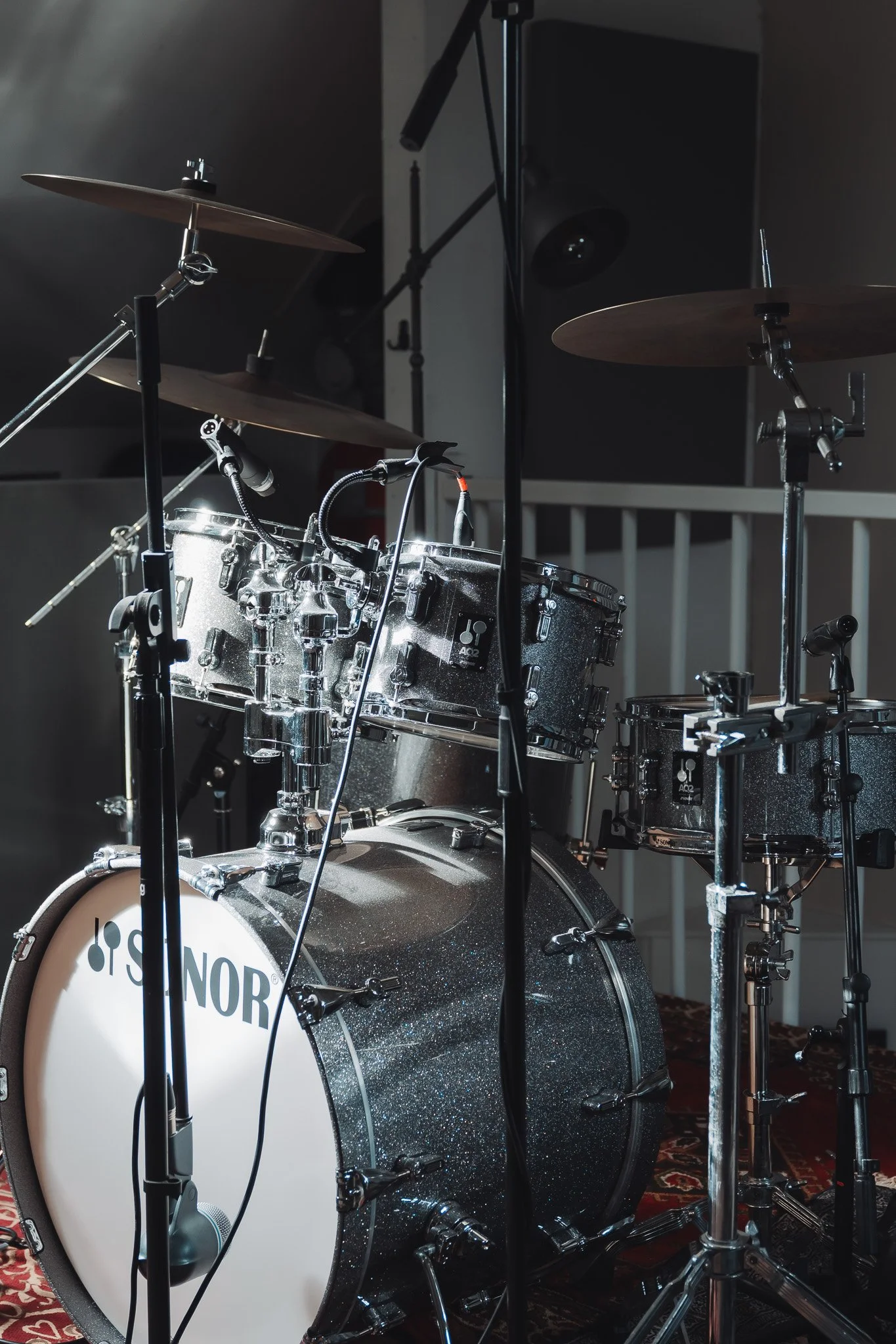 Een drumstel met zilverkleurige drums en cymballen, bevestigd aan standaards, op een tapijt in een kamer.