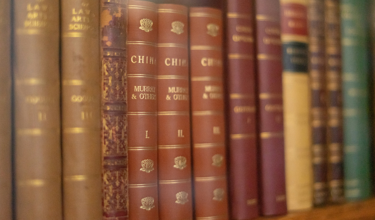 Shelf of old hardcover books with gold and embossed decorations on the spines.
