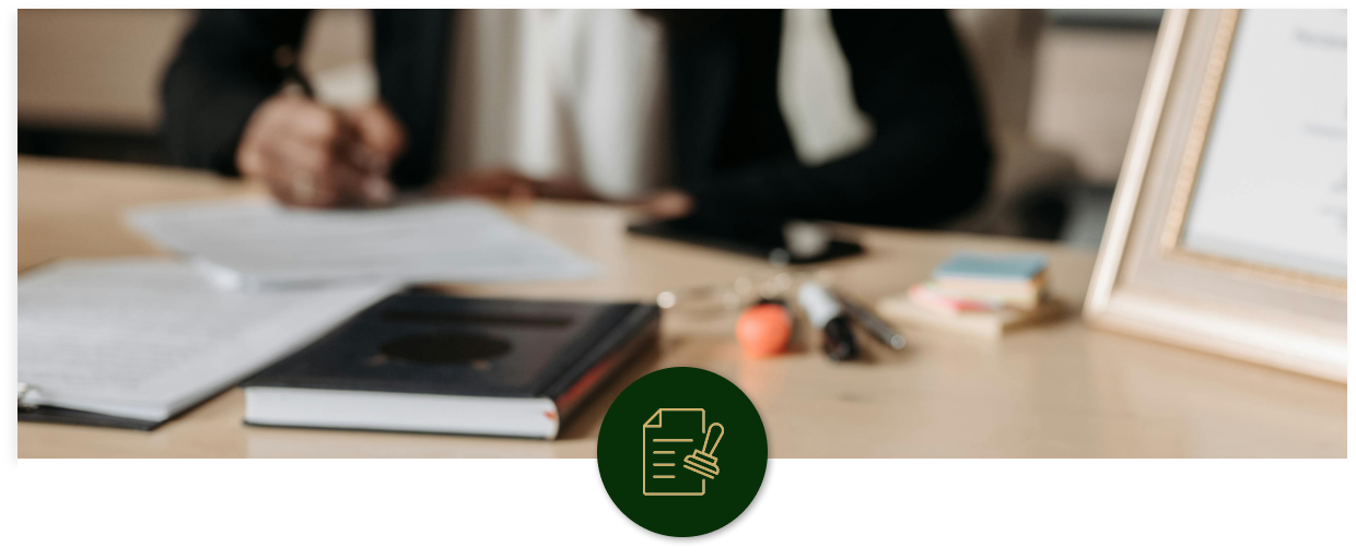 Person sitting at a desk with papers, a book, and office supplies, blurred background.
