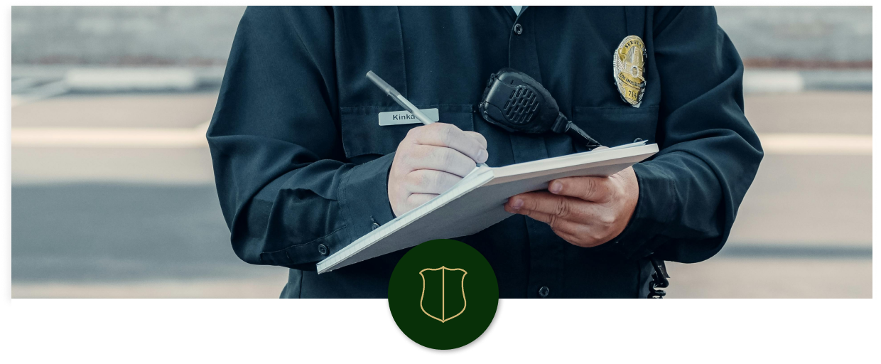 A police officer wearing a uniform and badge is taking notes on a notepad with a pen.