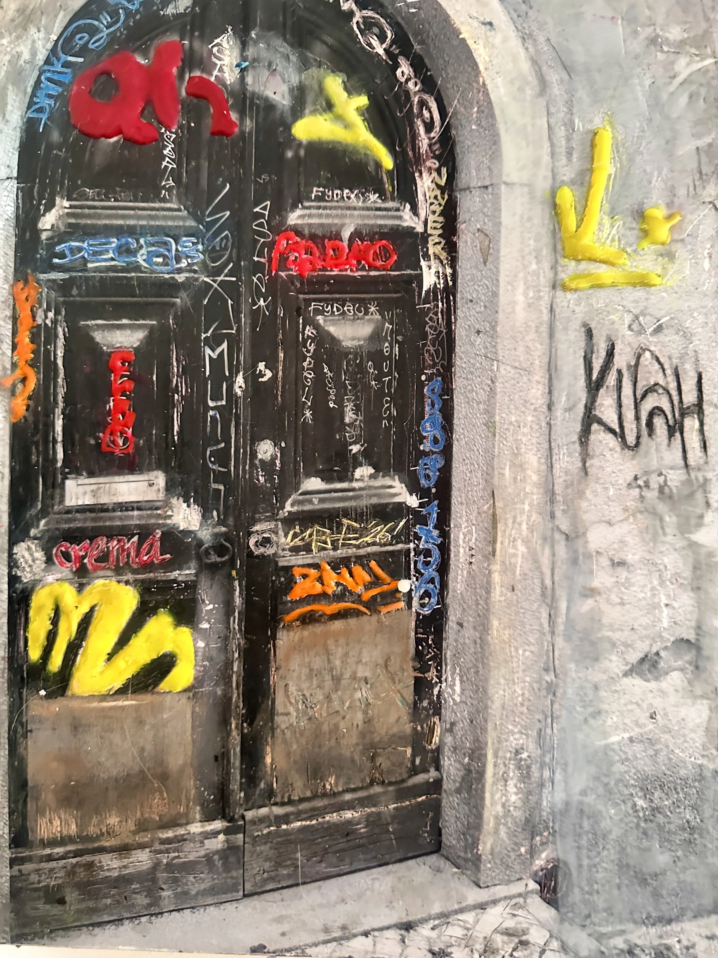 Graffiti-covered door and wall, with colorful spray paint including words and symbols on the door and wall.