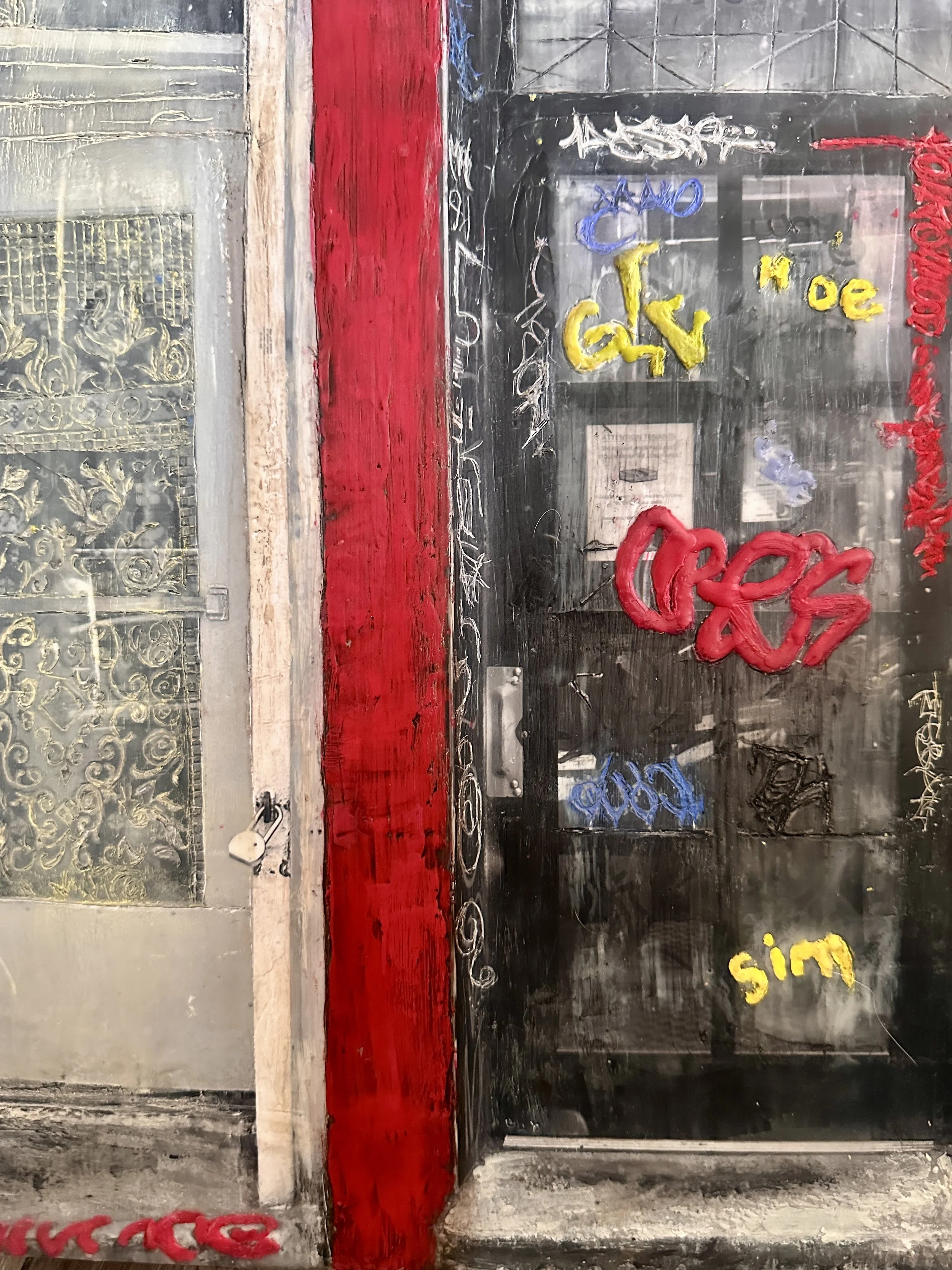 A black and gray metal surface with yellow, blue, red, and white graffiti, with a large red stripe running vertically, and a small yellow flower in the bottom right corner.