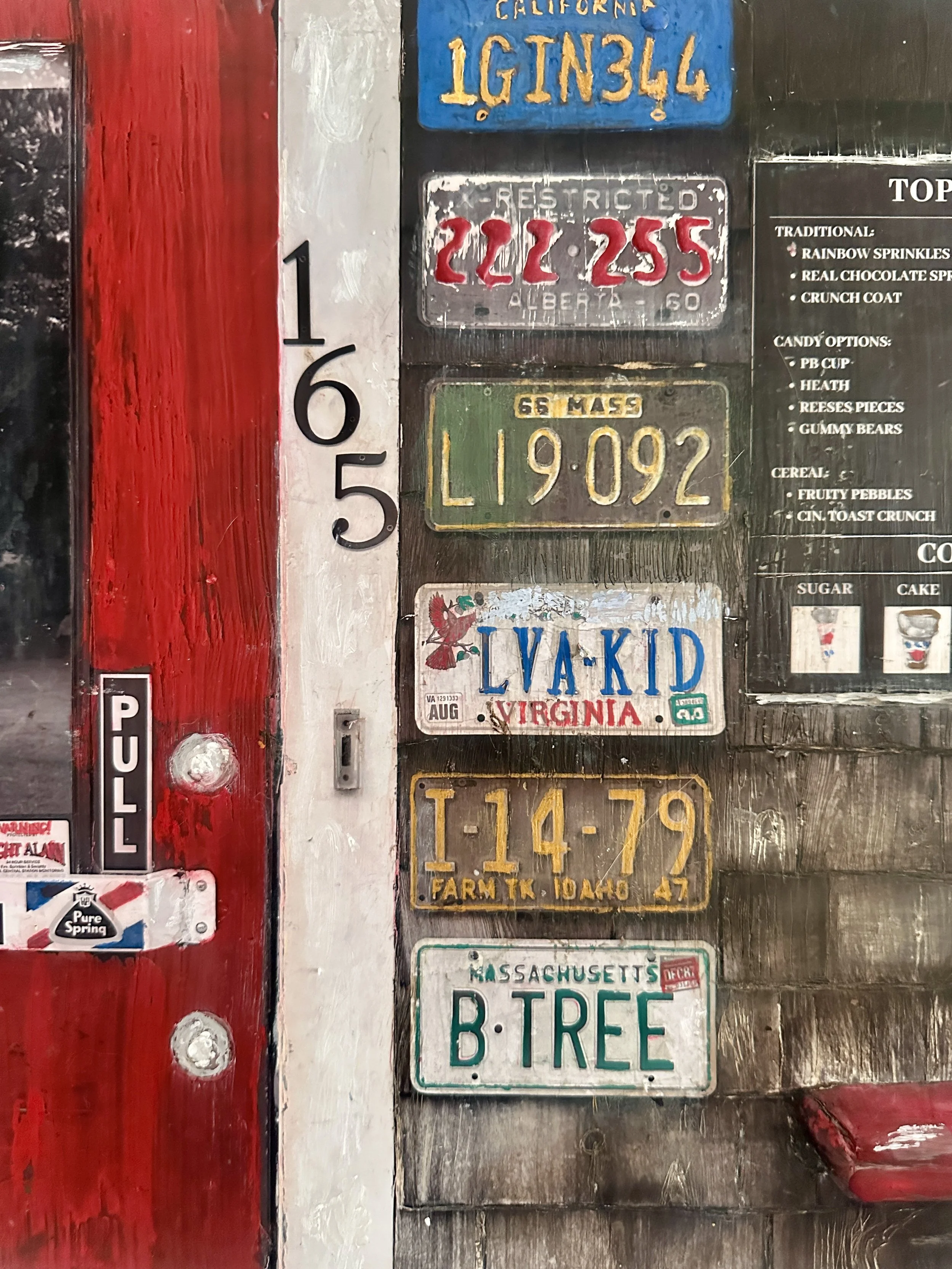 A collection of vintage license plates mounted on a weathered wooden wall, including tags from California, Virginia, Idaho, Massachusetts, and Idaho Farm.