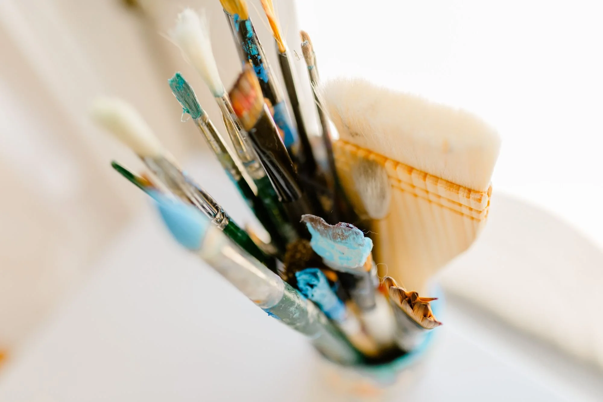 Close-up of paintbrushes with paint on their bristles, resting against a wooden brush holder.