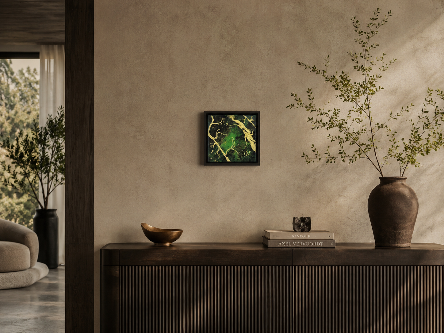 Interieur met een houten dressoir, een groene plant in een grote urn, een kunstwerk aan de muur, en een boekenstapel met een klein beeldje erop.