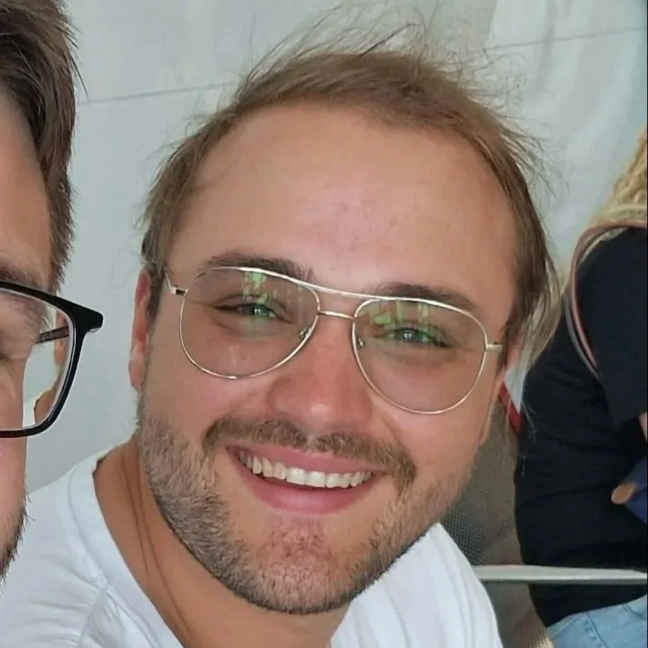 Lachende man met bril in een lichte kamer, op de foto genomen tijdens een sociale gelegenheid.