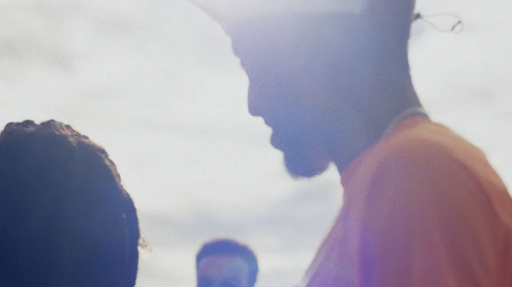 A close-up silhouette of a young woman and a young man facing each other outdoors with a cloudy sky in the background.