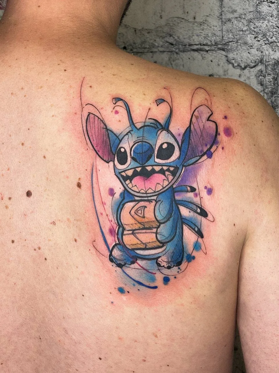 Colorful watercolor Stitch tattoo on the upper back by Maya Marina Tattoo.