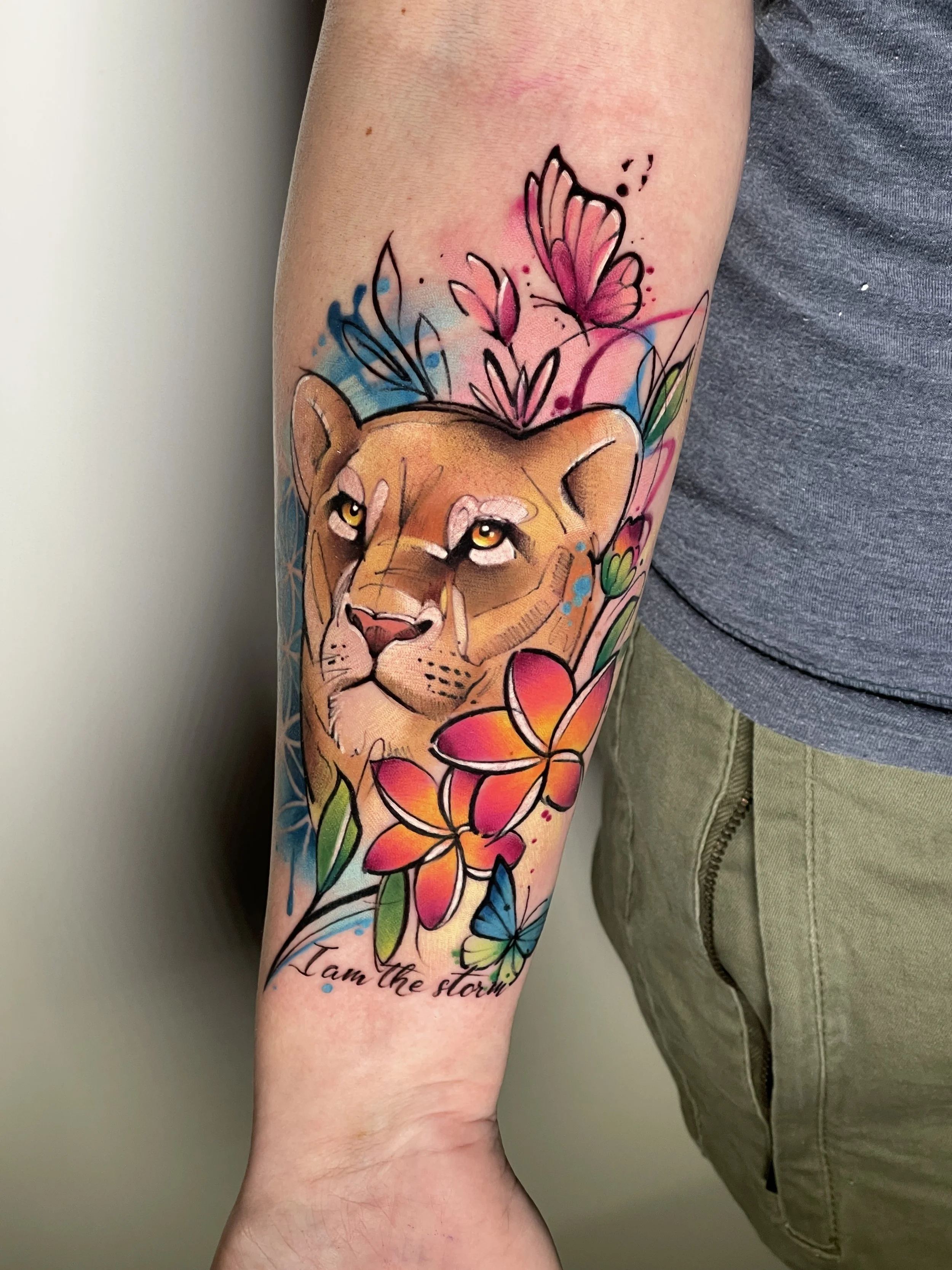 Colorful lioness tattoo with flowers and butterflies on the arm by Maya Marina.