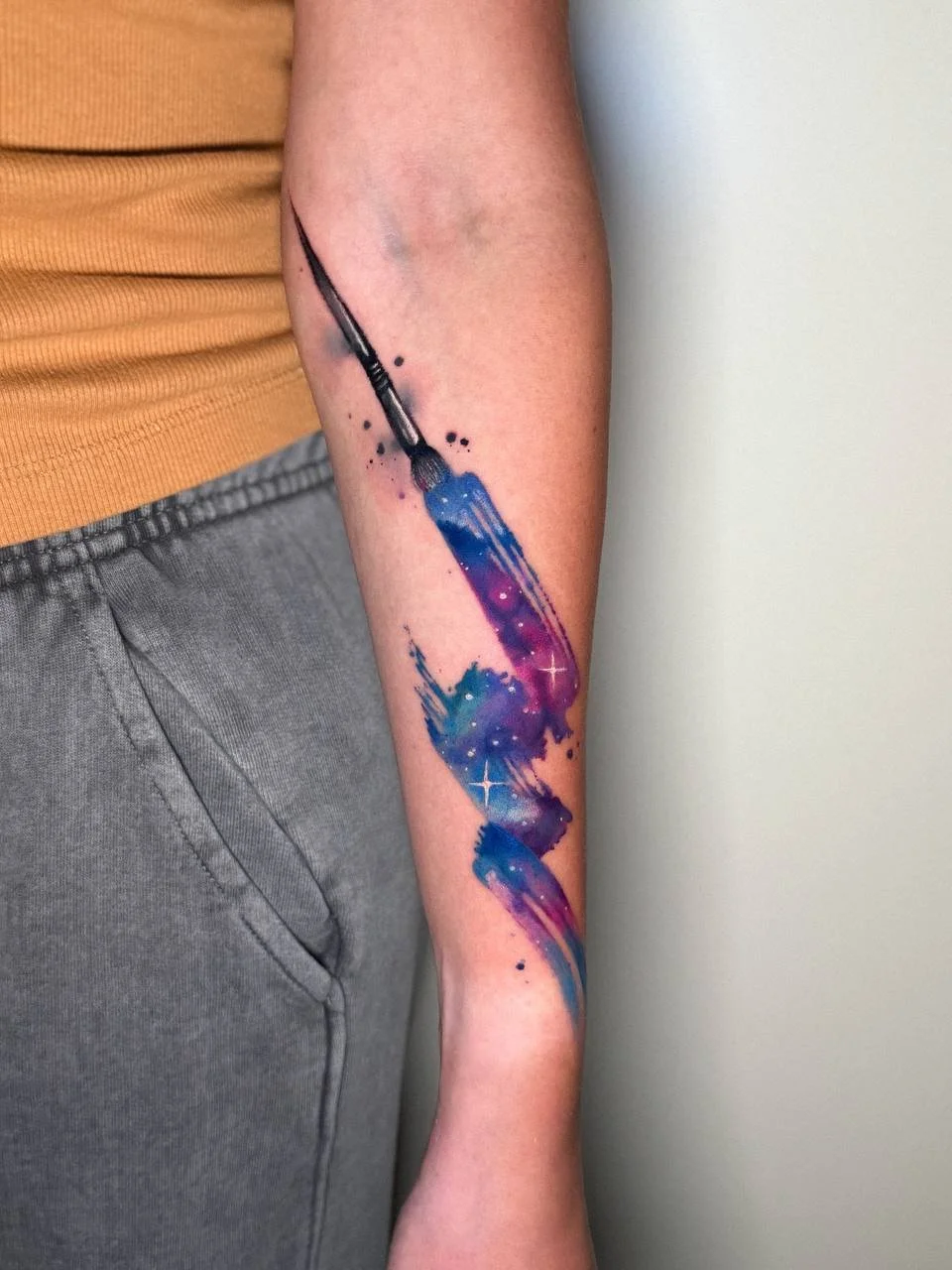 Abstract watercolor brushstroke tattoo in blue and pink tones on the arm by Maya Marina Tattoo.