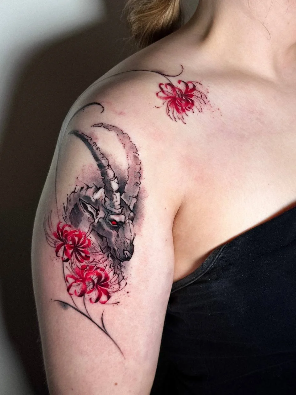 Artistic sketch-style goat tattoo with red flowers on the shoulder by Maya Marina Tattoo.