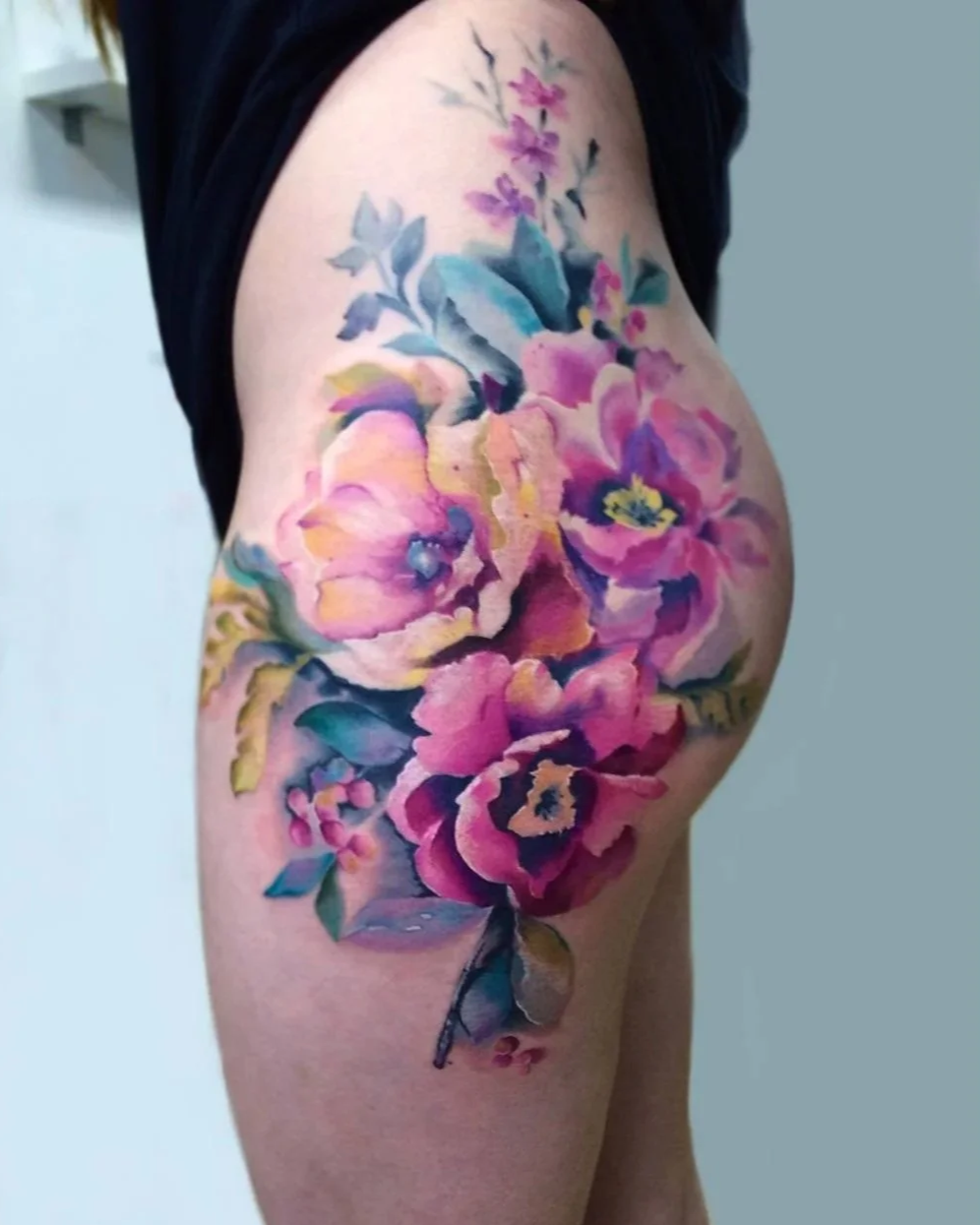 Colorful floral thigh tattoo with pink and purple flowers by Maya Marina.