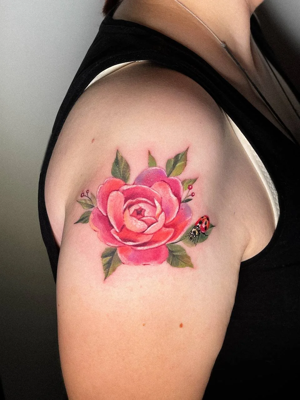 Kleine Aquarell-Tätowierung mit einer rosa Pfingstrose und einem Marienkäfer auf der Schulter.