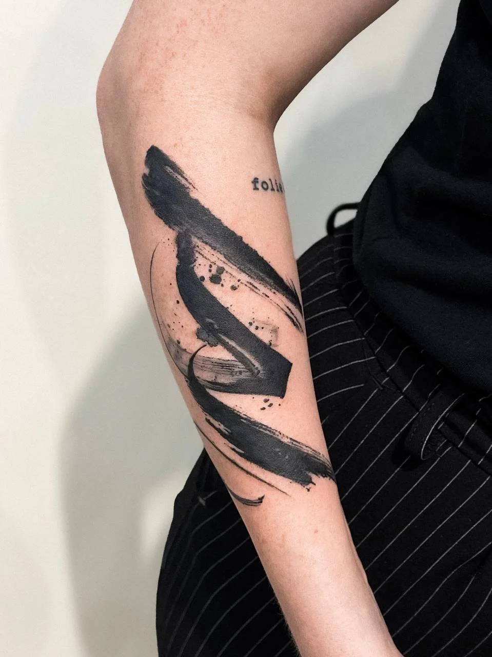 Kleines abstraktes Tattoo in Schwarz mit expressiven Pinselstrichen