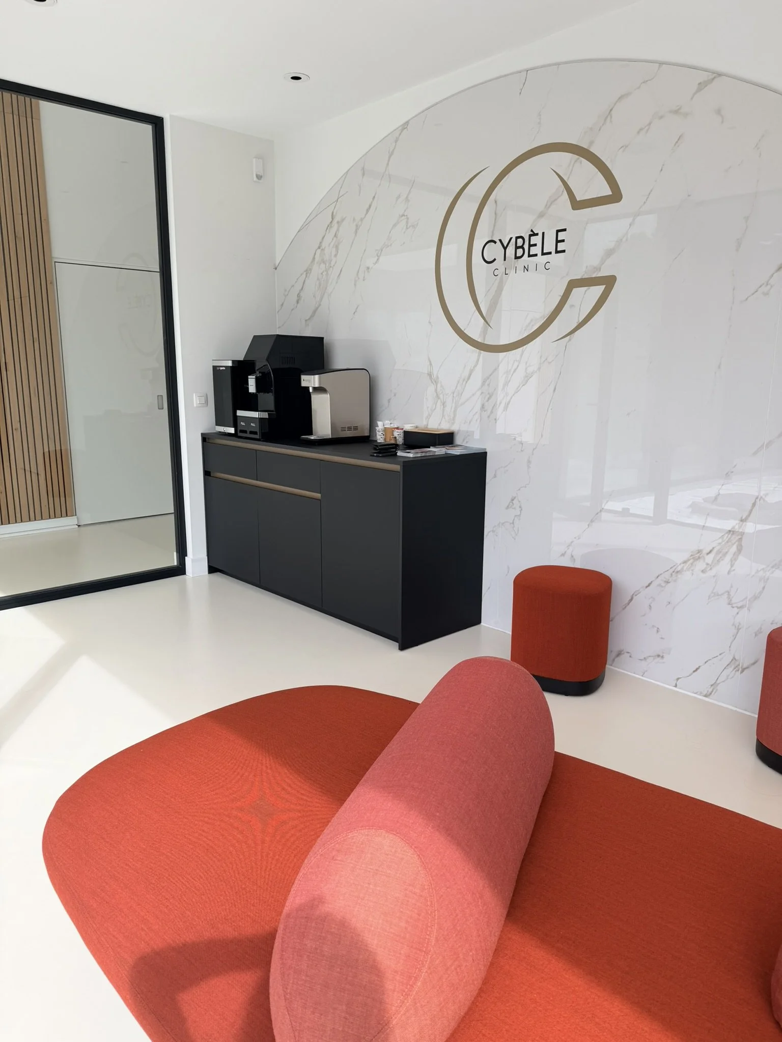 Intérieur moderne de cabinet médical avec un grand fauteuil orange et un mur en marbre blanc, logo CYBÈLE CLINIC visible.