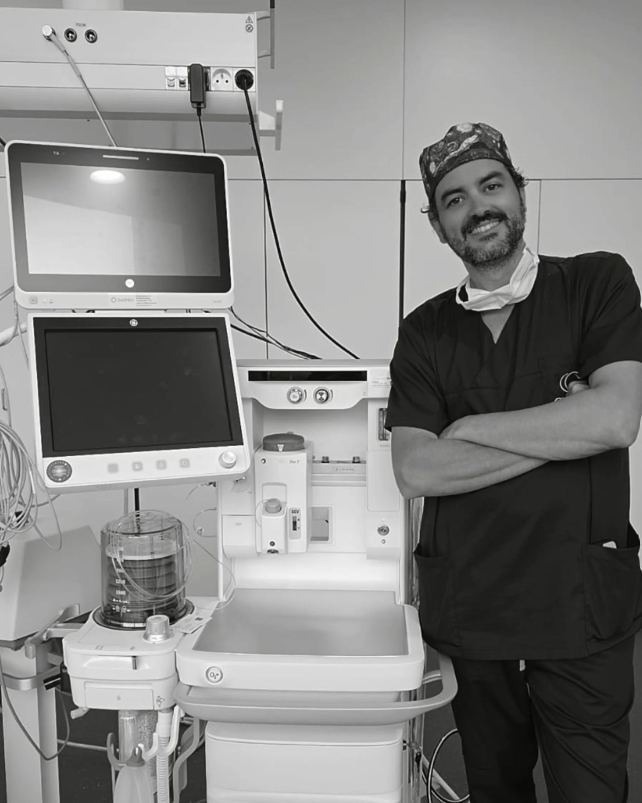 Le Dr Bruno Vanderbeck, anesthésiste, en tenue médicale souriant dans une salle d'hôpital, entouré d'équipements médicaux, y compris des moniteurs et des appareils de surveillance médicale.