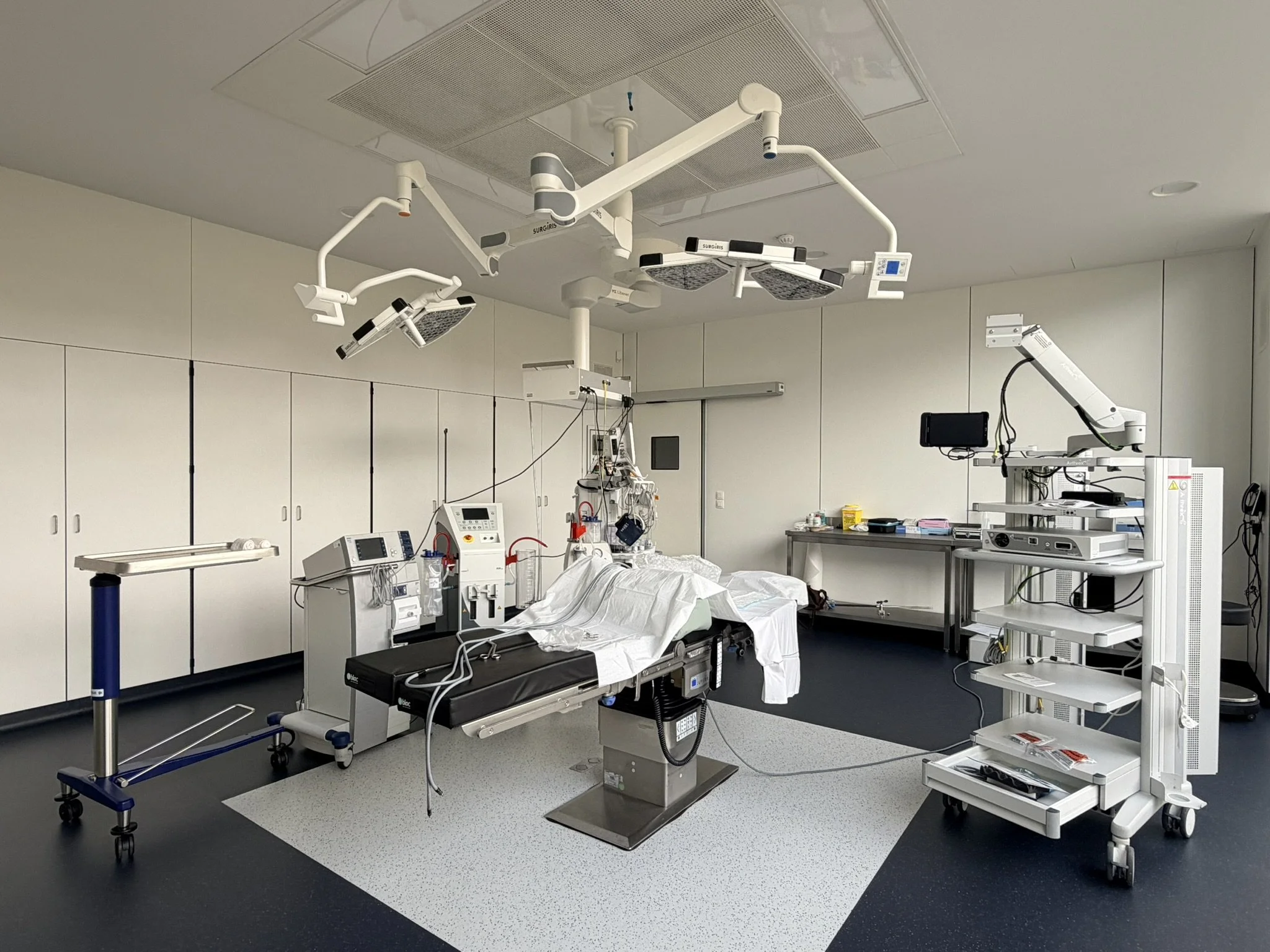 Une salle d'opération chirurgicale équipée de luminaires, d'un lit d'hôpital, et divers appareils médicaux, prête pour une intervention.
