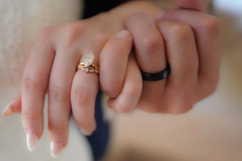 Close-up of two hands with rings, one with an engagement ring featuring a large diamond, and the other with a black wedding band.