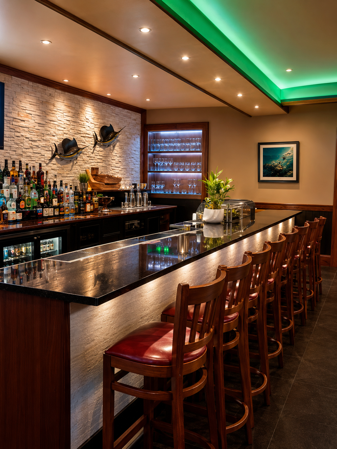 Empty bar with a black marble counter, wooden bar stools with red cushions, liquor bottles, wine glasses, a plant in a white pot, and decorative fish sculptures on a textured brick wall.