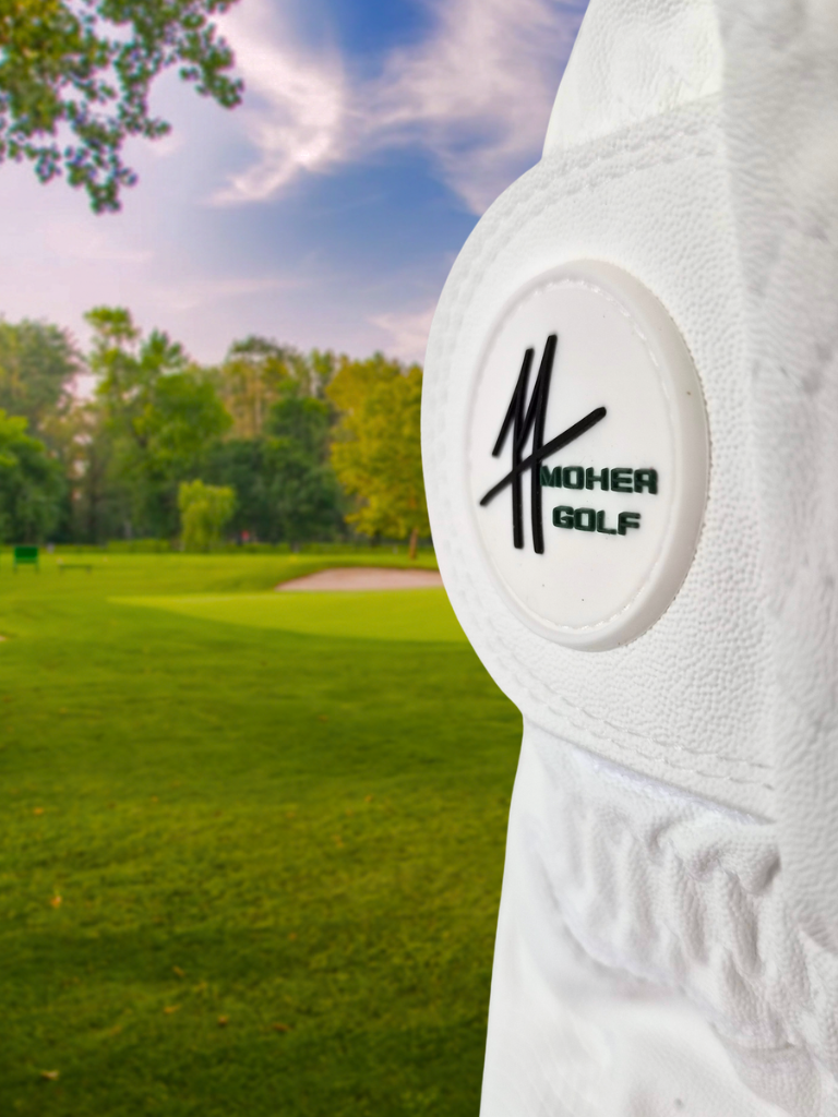 Moher Golf white all-weather leather golf glove featuring the raised Moher Golf logo tab on a lush golf course green.