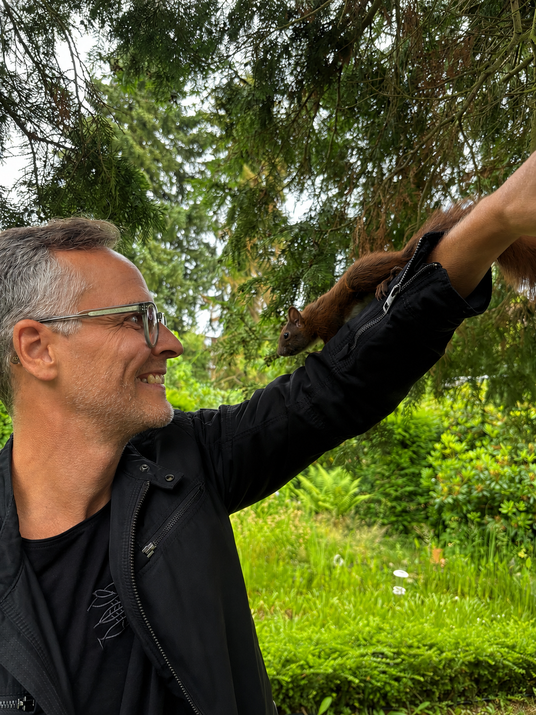 Lachender Mann mit Eichhörnchen an einer Außenvoliere.