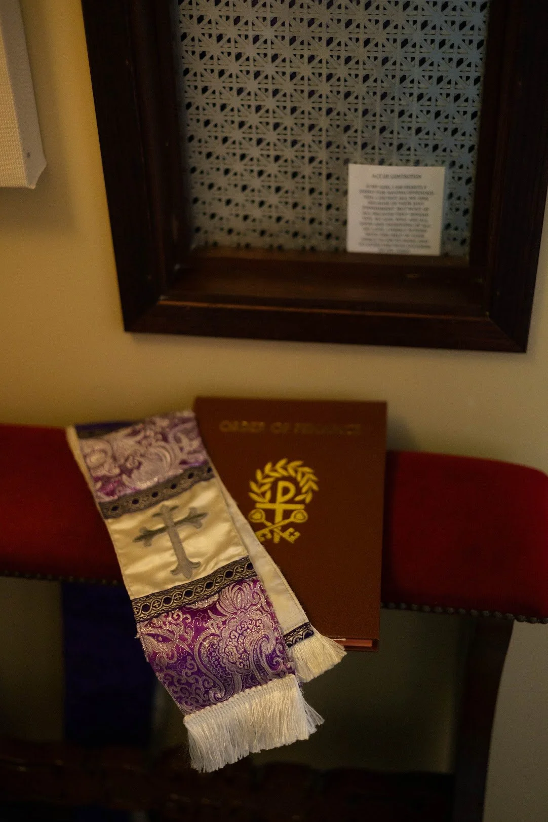 Religious display on a table with a purple and white cloth with a cross, an open book with a gold emblem, and a framed note on the wall behind.