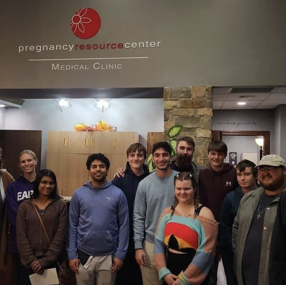 Group of people smiling inside a pregnancy resource center medical clinic, with a stone pillar and wood cabinets in the background.