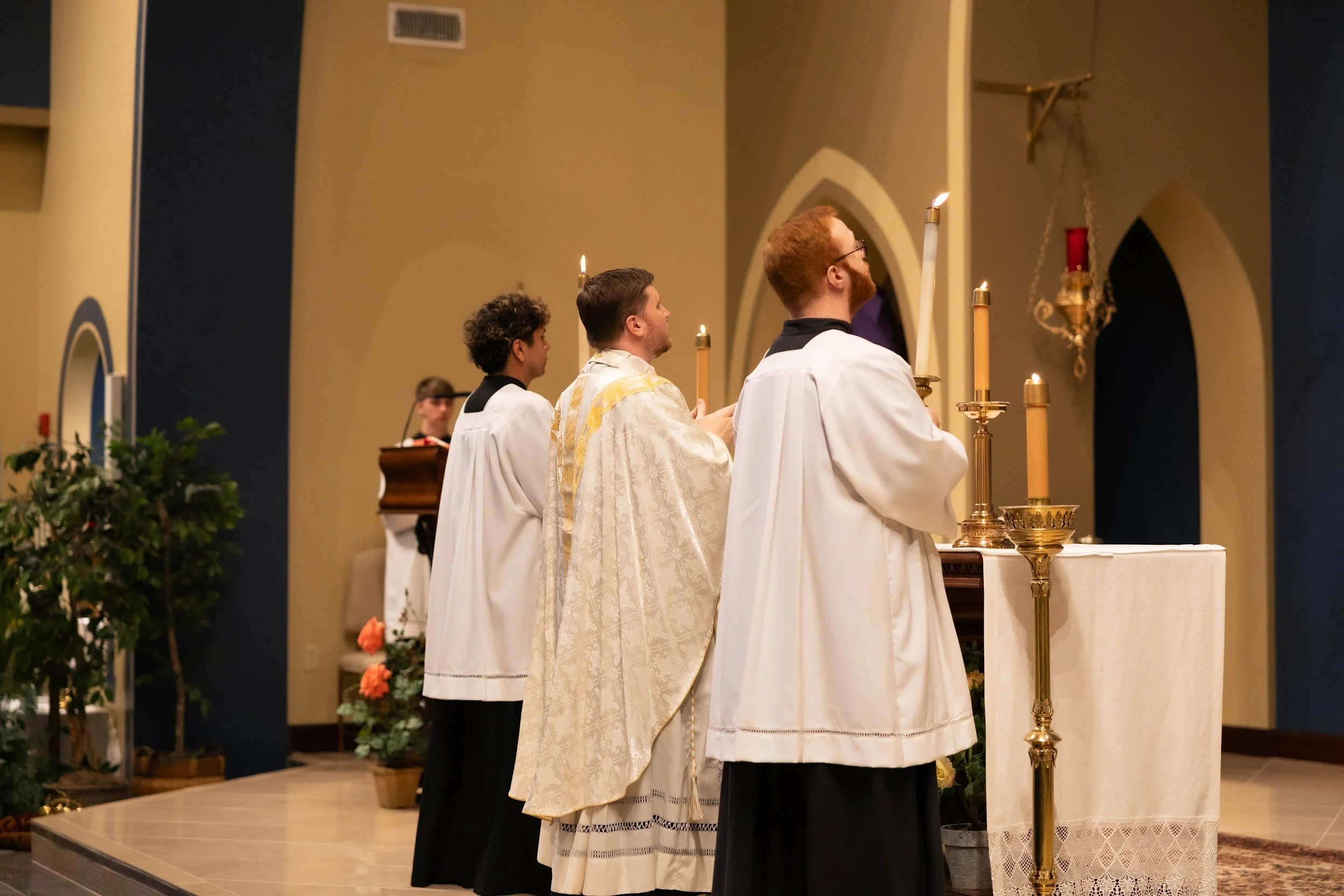 Three clergy members dressed in white robes standing in front of an altar during a religious ceremony inside a church.