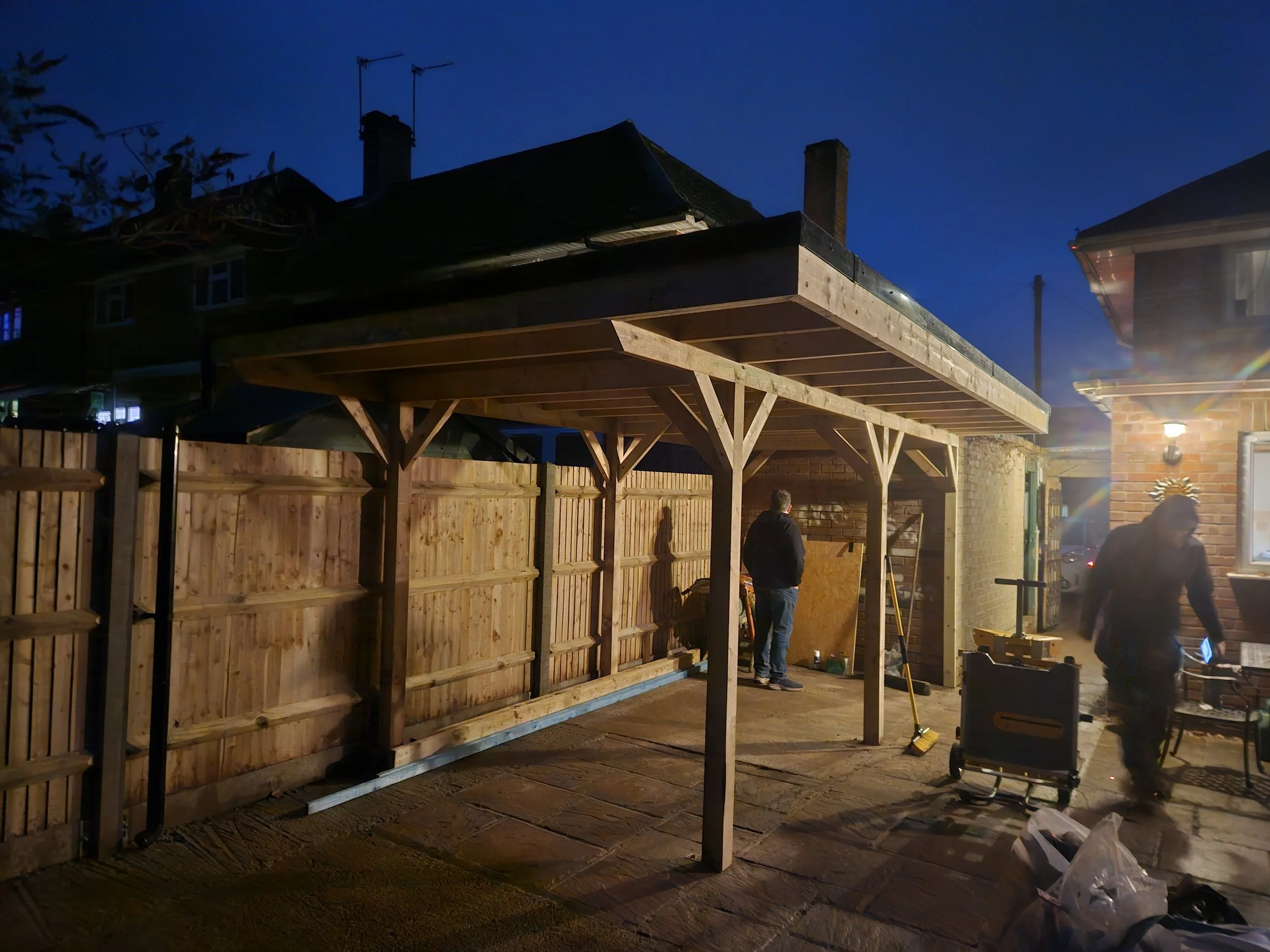 People building a wooden fence outside at night with construction tools and materials around.