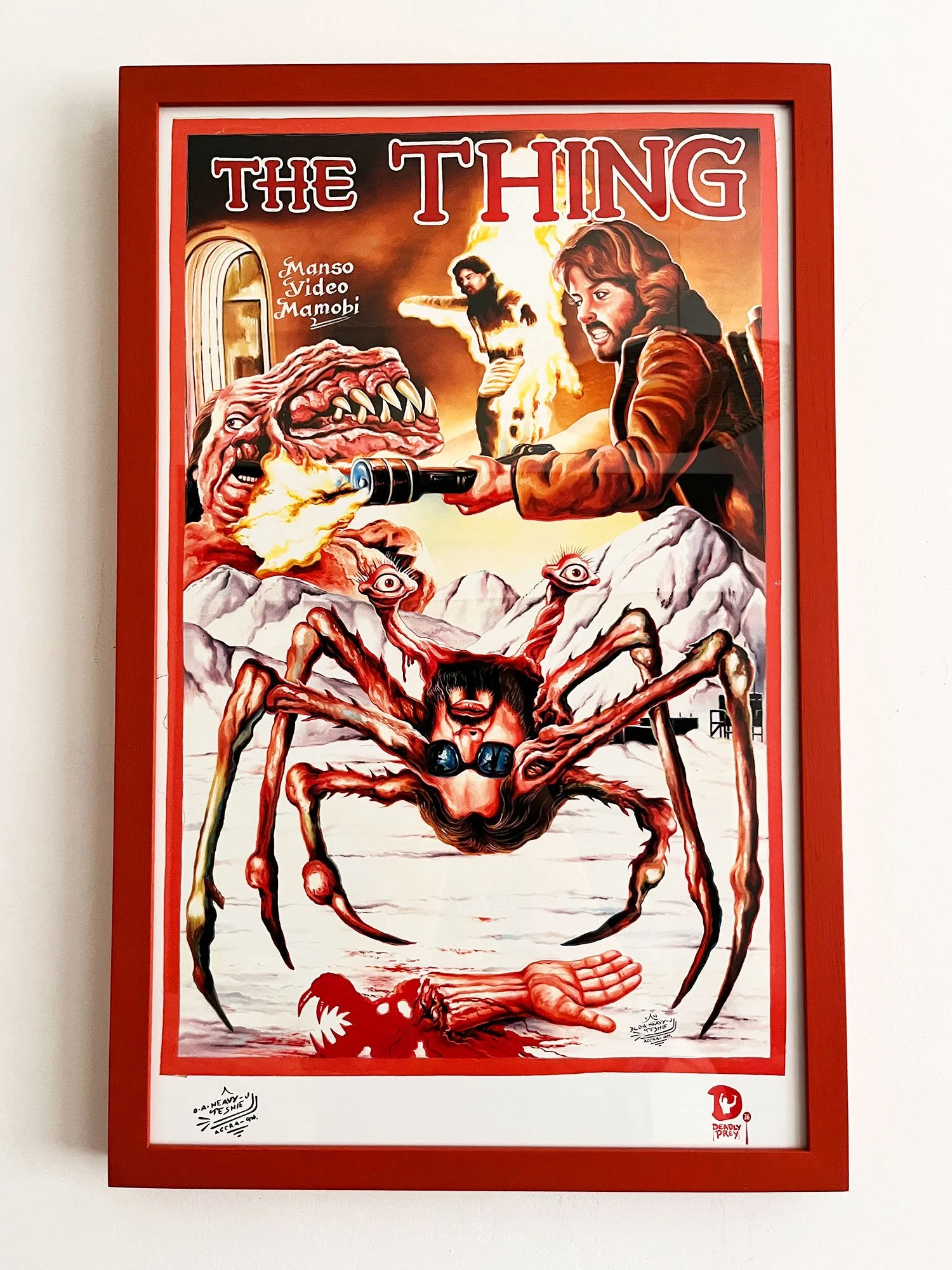 A illustrated poster for the movie "The Thing:  The poster is framed in an orange frame, includes multiple illustrations of creatures, the text that reads 'THE THING', and includes 'Manso Video Mamobi' and 'Deadly Prey' logos.