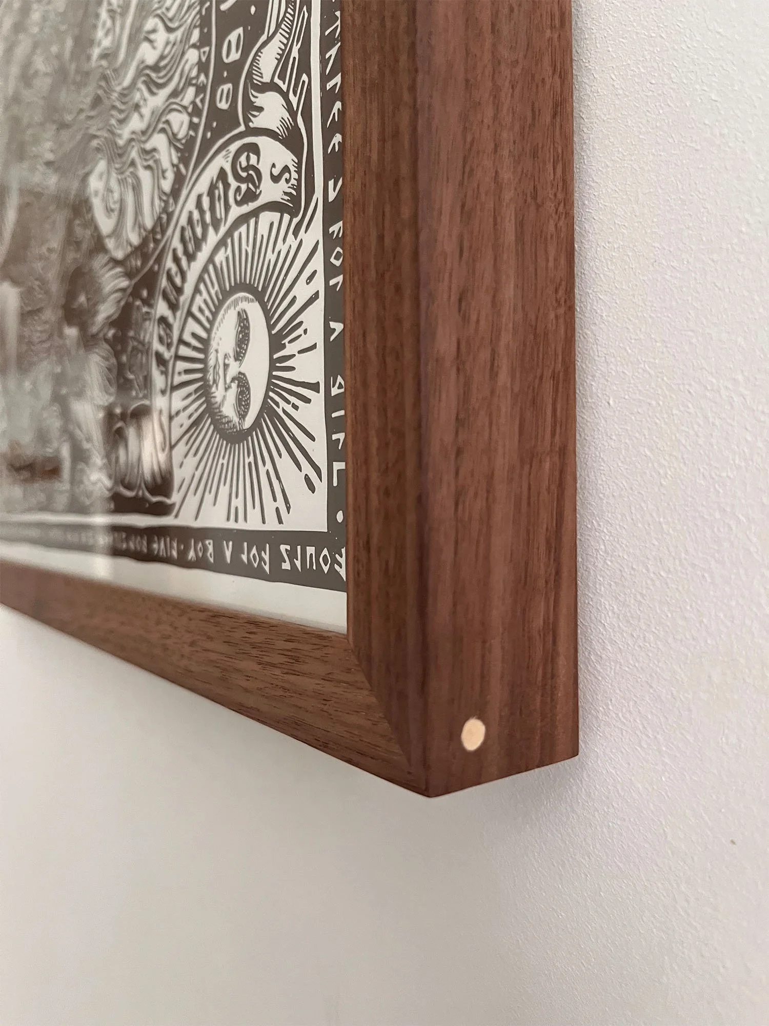 Close-up of a walnut wooden frame surrounding a black and white graphic poster on a white wall.
