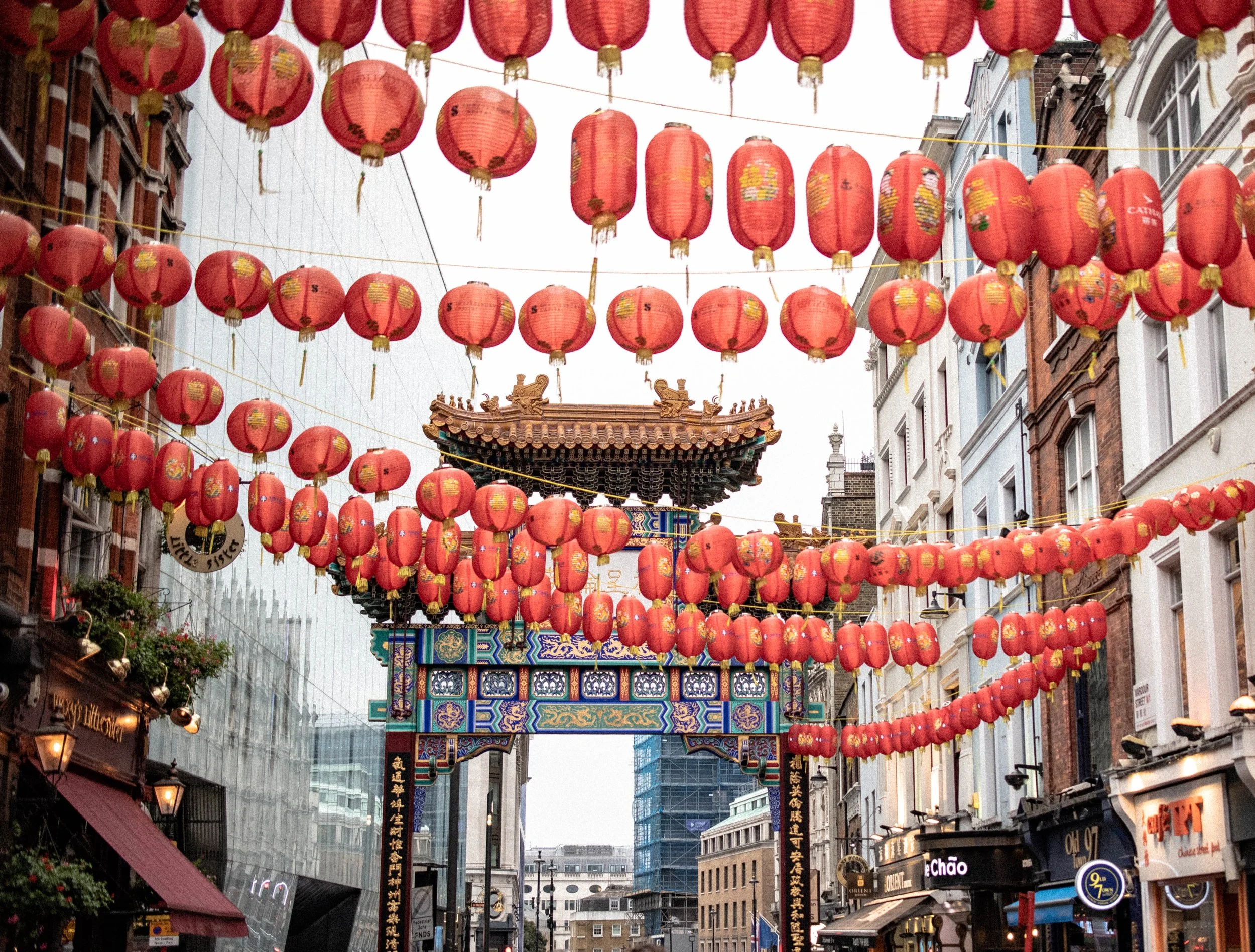 Street decorated with multiple rows of red lanterns hanging above during a festival, with traditional Chinese architecture and modern buildings in the background.