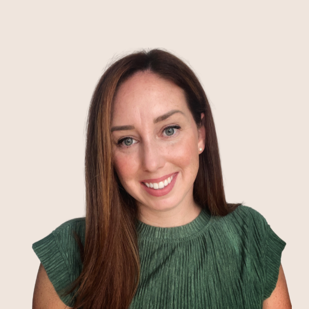 A woman with long, straight auburn hair and blue eyes smiling, wearing a green top with ruffled sleeve details, against a plain beige background.