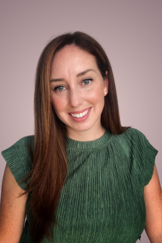 A woman with long brown hair smiling, wearing a green top with ruffled sleeves, in front of a light purple background.