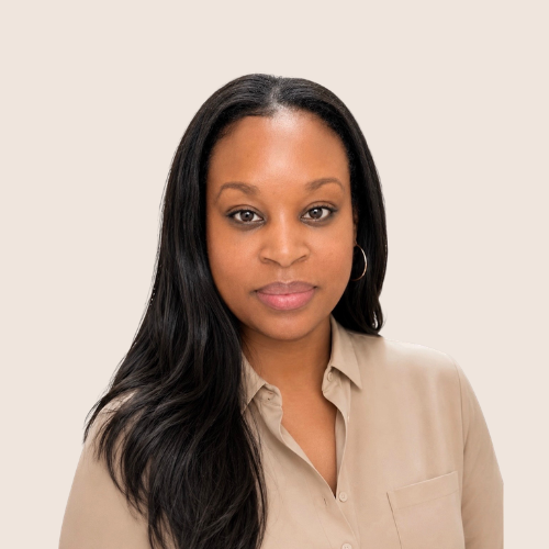 A woman with long black hair, wearing a beige shirt and hoop earrings, looking at the camera against a plain light-colored background.