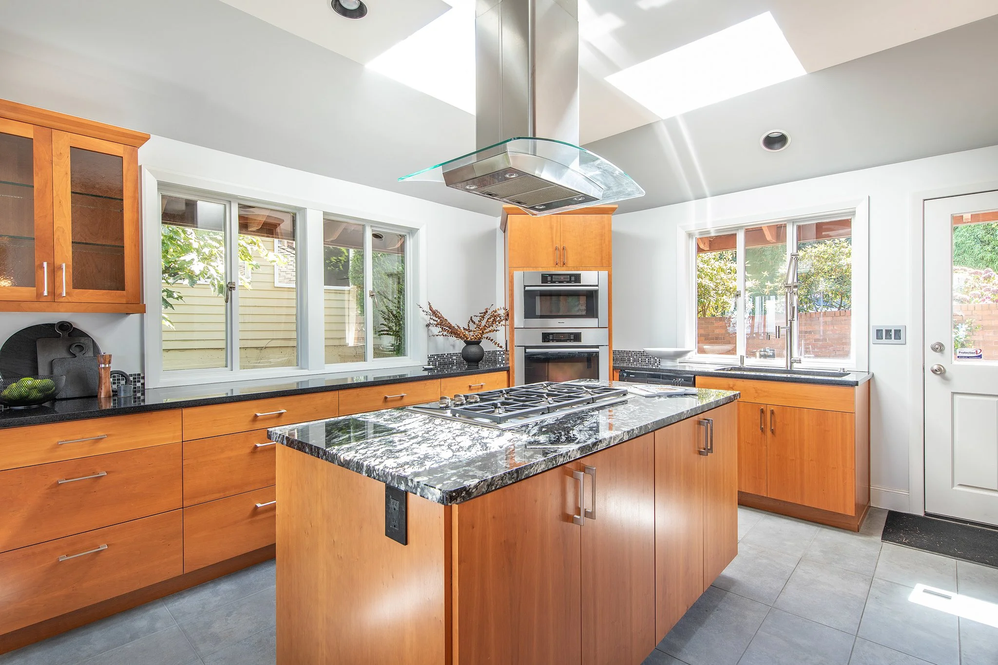 Modern kitchen with wooden cabinets, granite countertop, stainless steel appliances, large windows, and a skylight providing natural light.